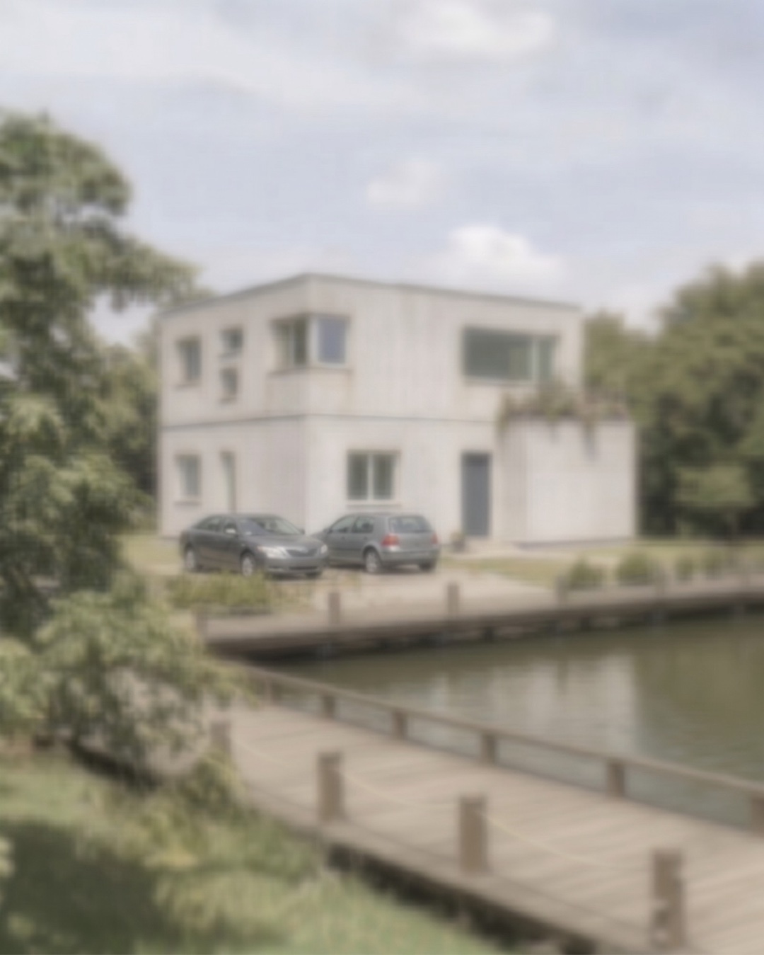 The same lakeside site built the conventional way: a flat-roofed white box with cars parked in front.