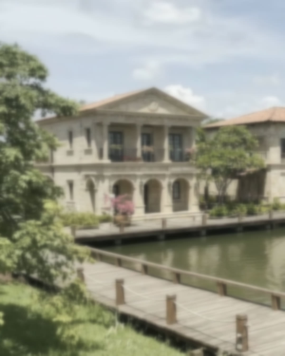 Concept visualisation: a classical stone villa with a pedimented portico beside a lake, reached by a timber boardwalk.